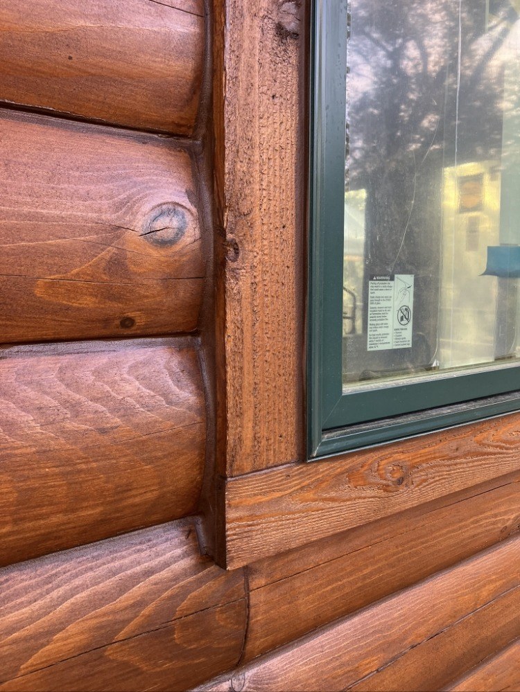 Energy seal applied along window trim and log lines on a stained log wall