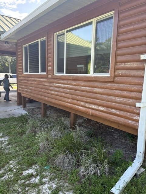Log home siding with failing stain peeling away from the logs before restoration