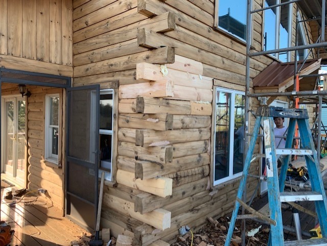 Replacement logs being fitted into a log home wall with scaffolding in place