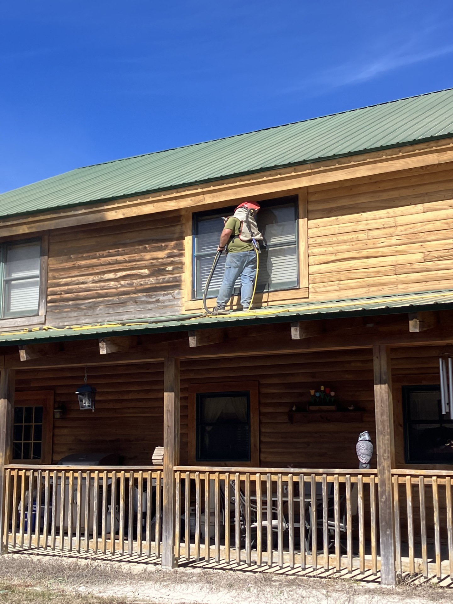 Crew member in protective gear media blasting old finish off a log home wall