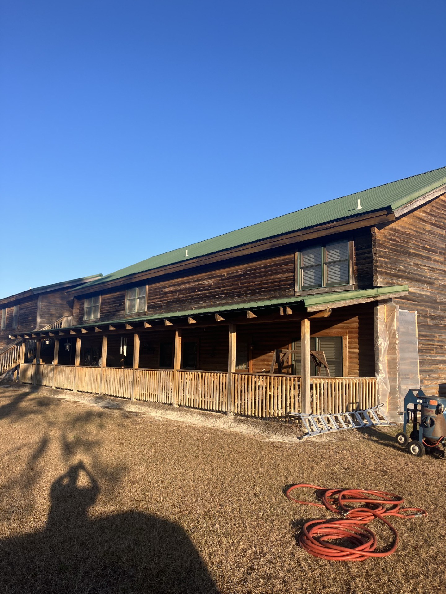 Long porch elevation of a log home stripped by media blasting, with blast hoses on the ground