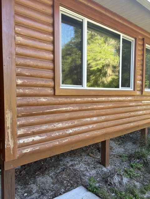 Close-up of log siding where the old stain has peeled off, exposing bare gray wood