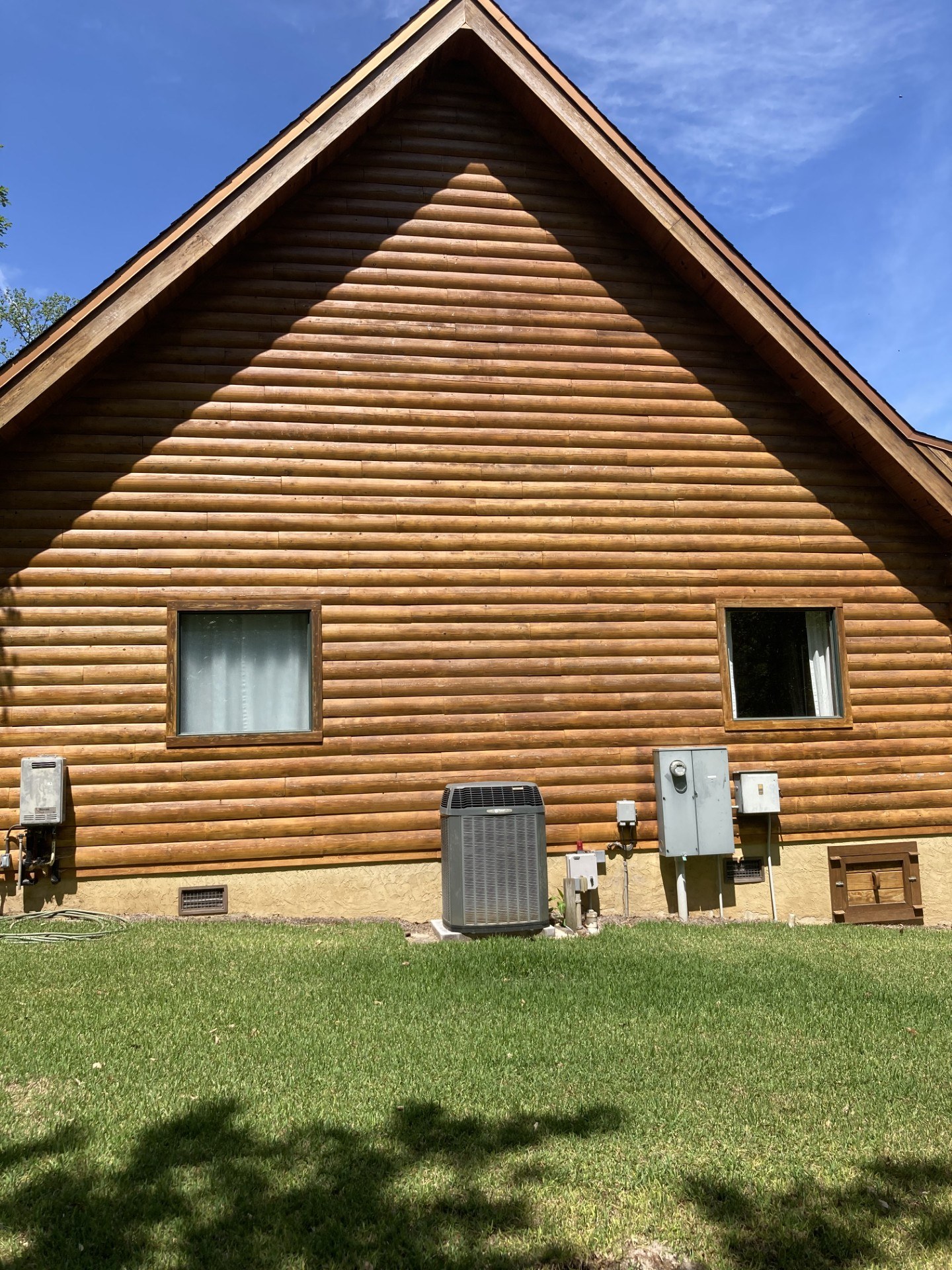 Log home gable finished in a warm honey tone above a stucco foundation