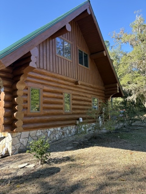 Restained log home gable above a stone foundation with a green metal roof