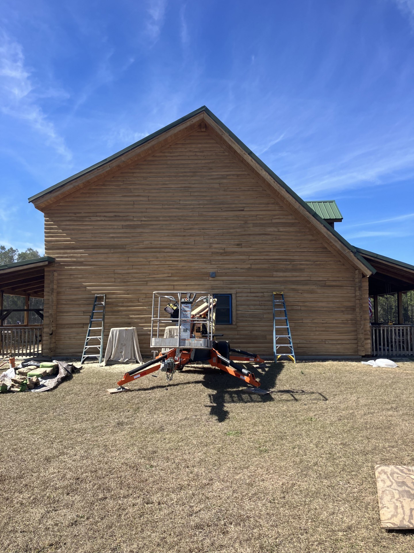 Boom lift and ladders staged against a log home during a restaining project
