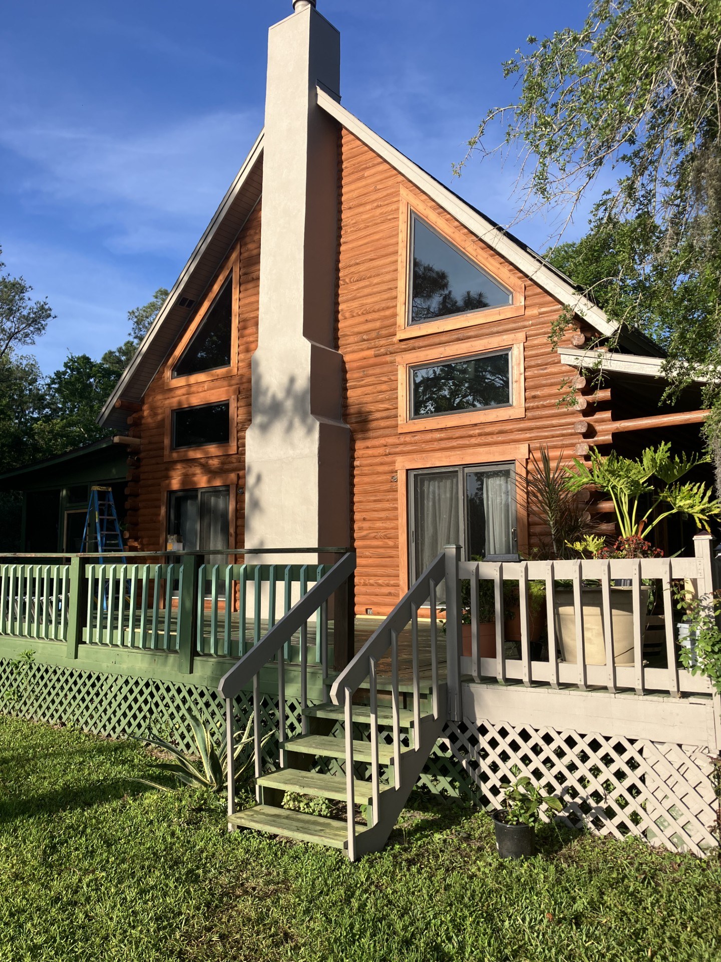 Gable end of a restored A-frame log home above a painted deck and steps