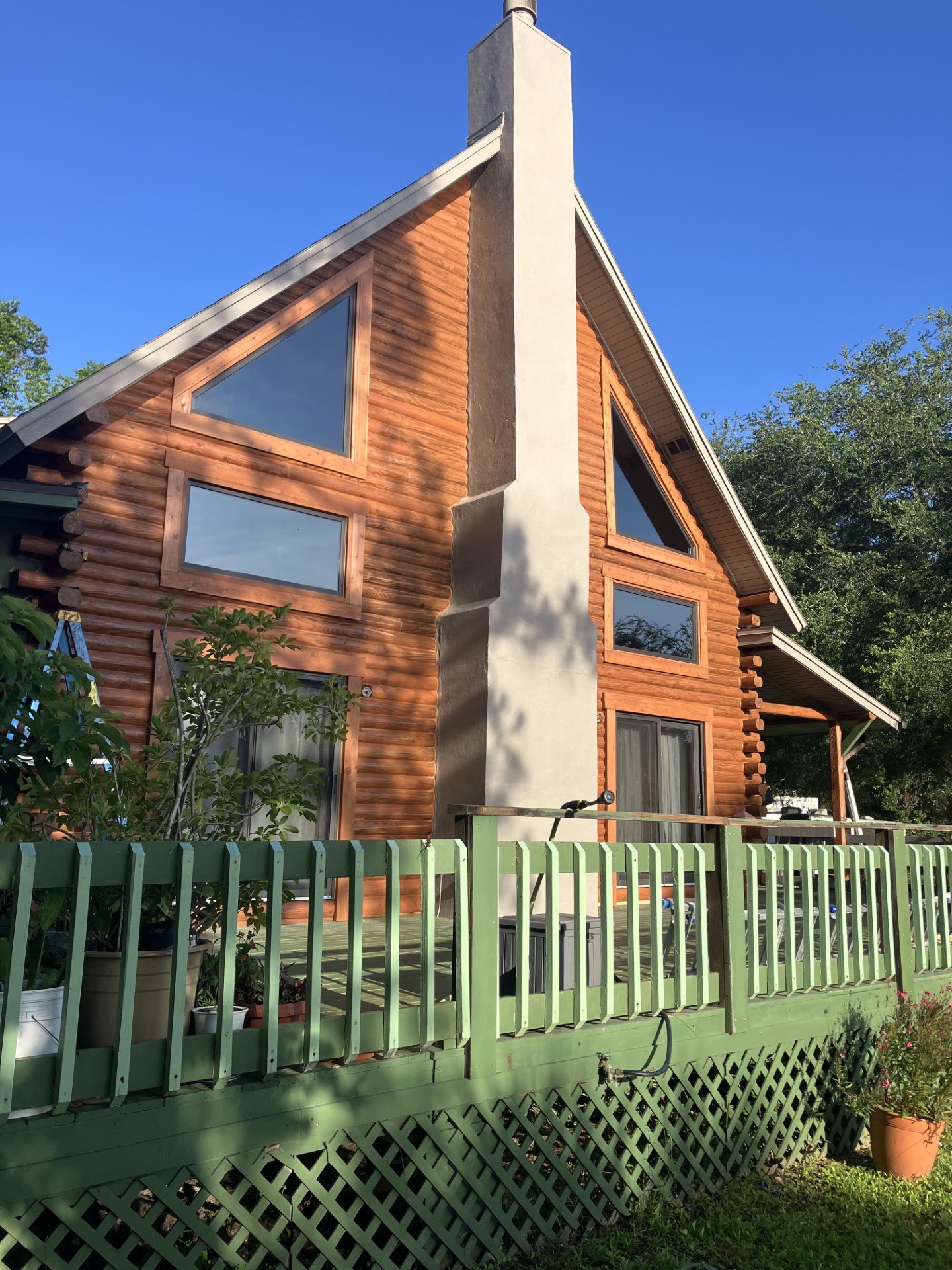 Restored A-frame log home with a masonry chimney and a painted wraparound deck