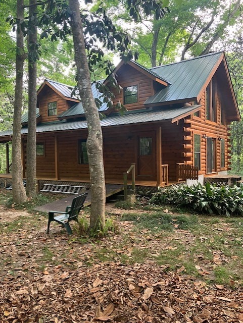 Restored log cabin with dormers and a metal roof surrounded by trees