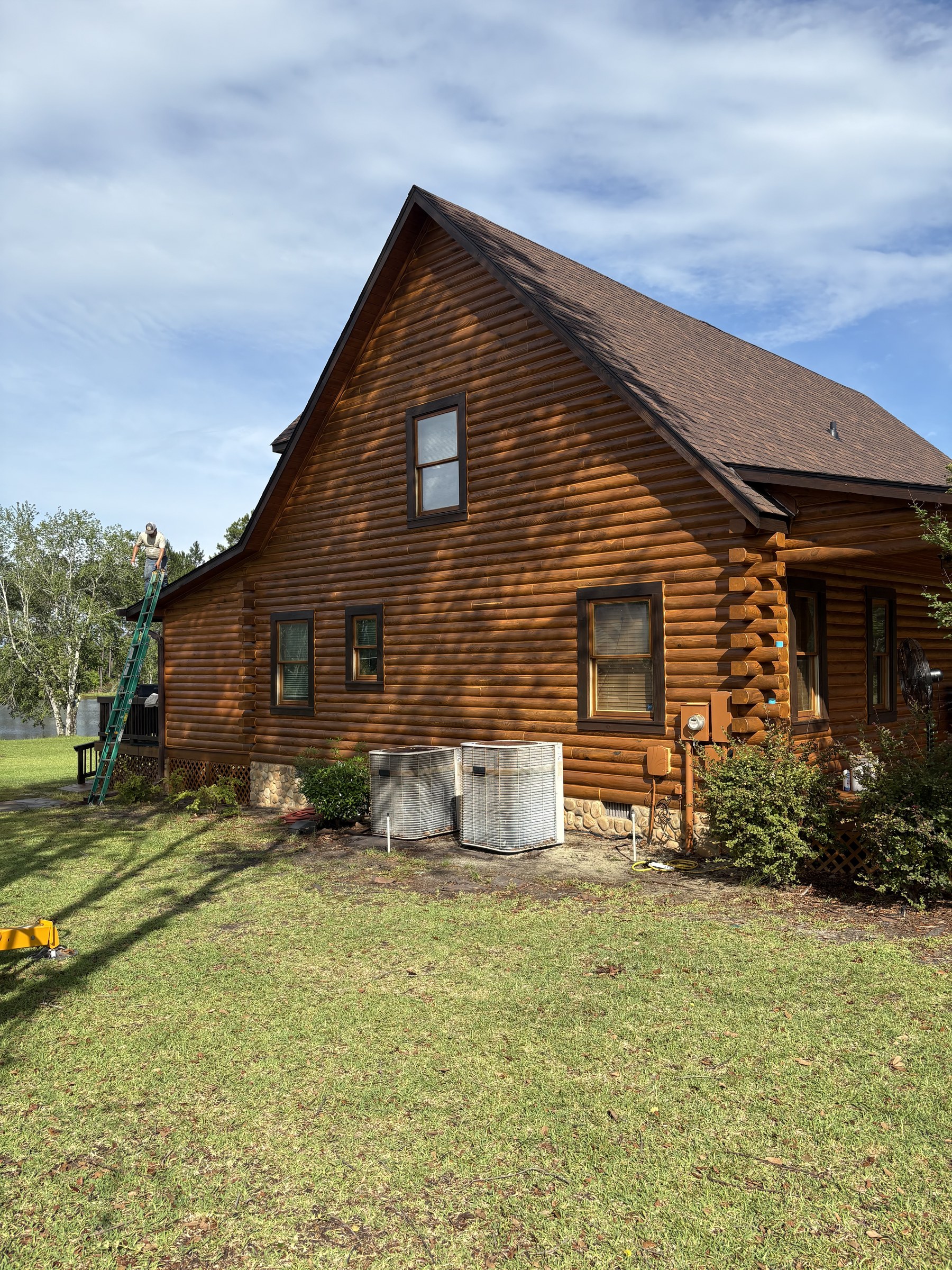 Crew member on a ladder working the side elevation of a restored log home