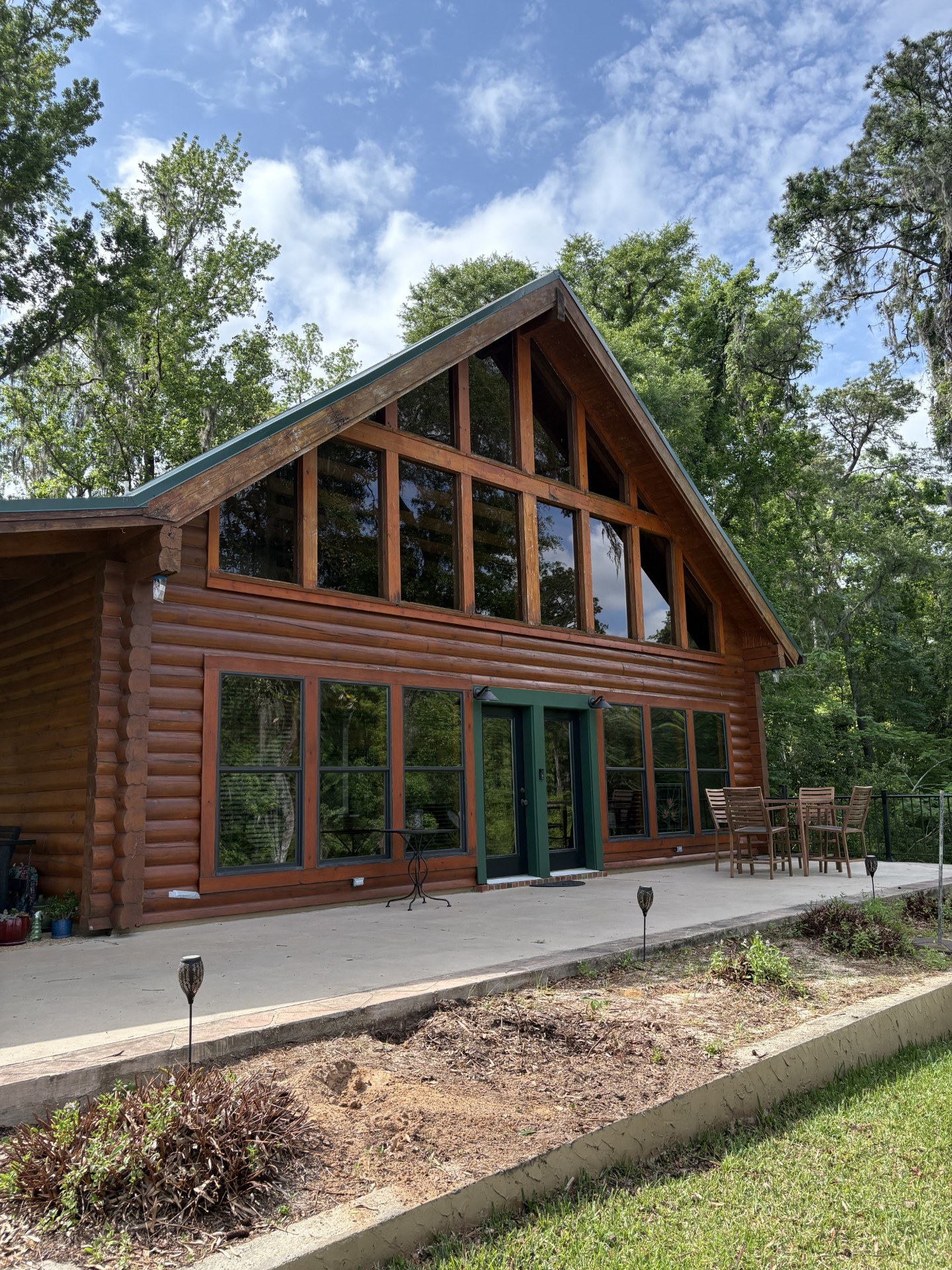 Restored log home with a tall window wall and patio beneath a green metal roof