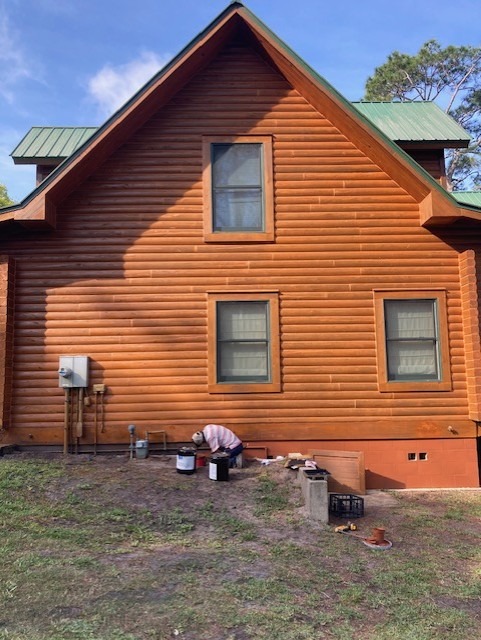 Crew member applying fresh stain to the gable end of a log home
