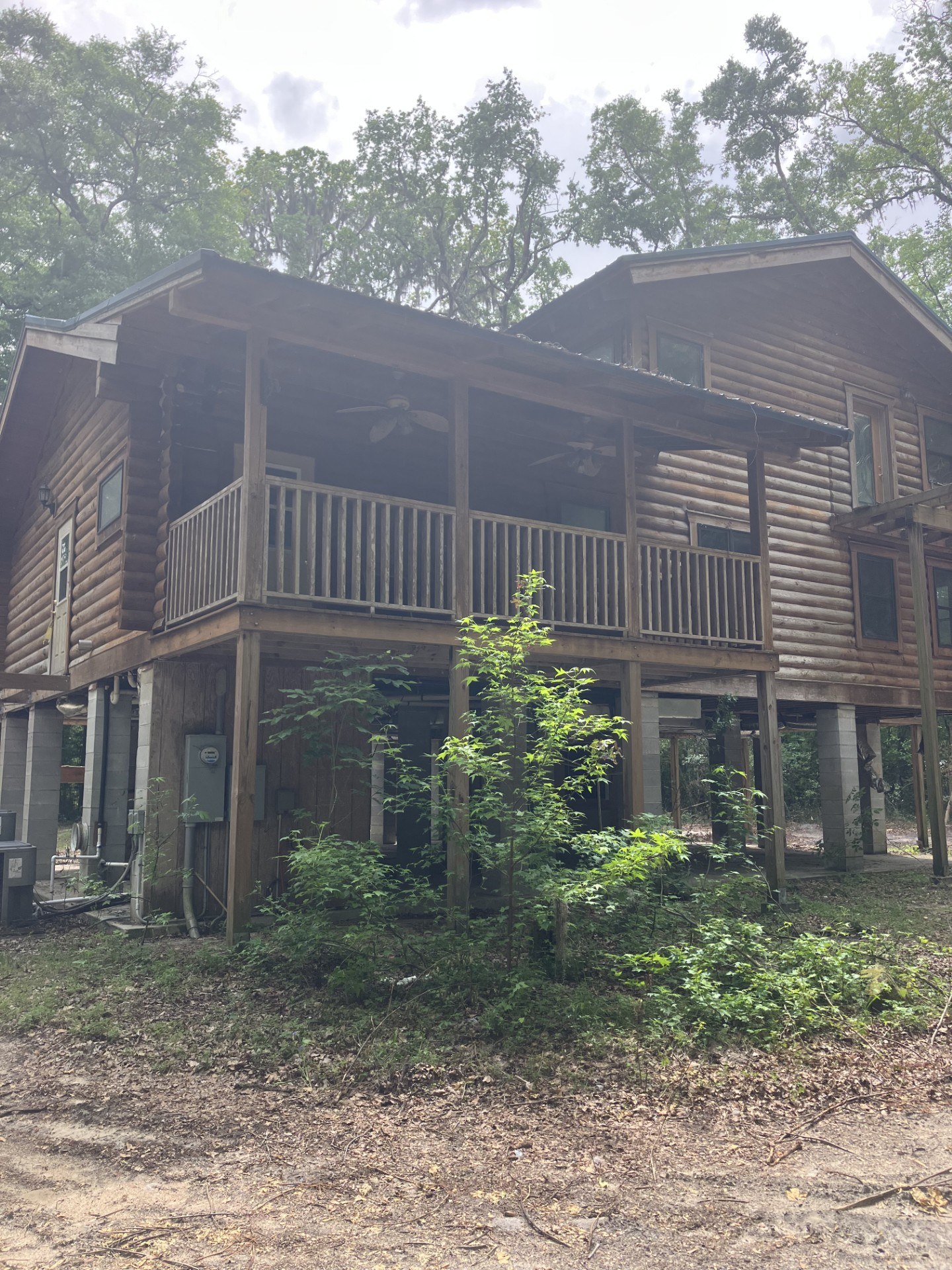 Weathered elevated log home in the woods, dull and graying before restoration