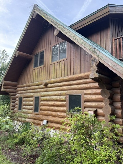 Weathered log home with graying logs and algae growth along the roofline before restoration